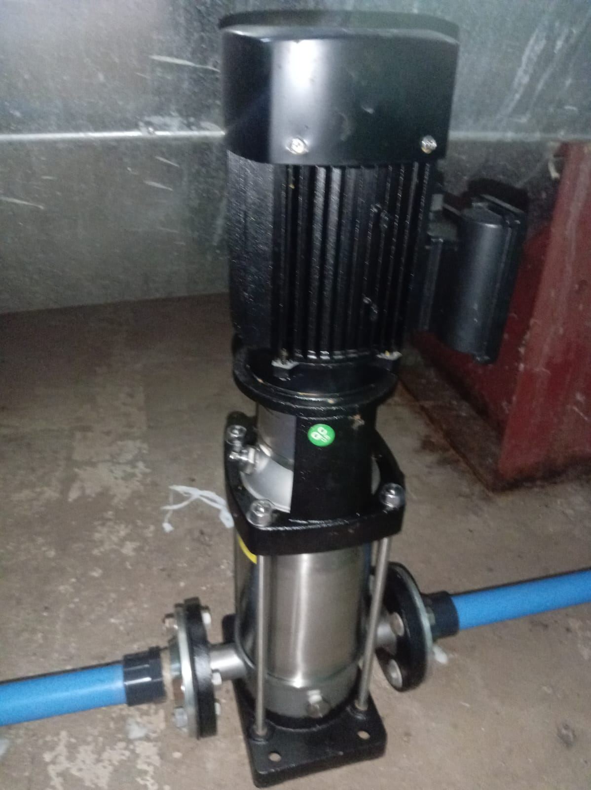 A vertical water booster pump with blue pipework connected on both sides