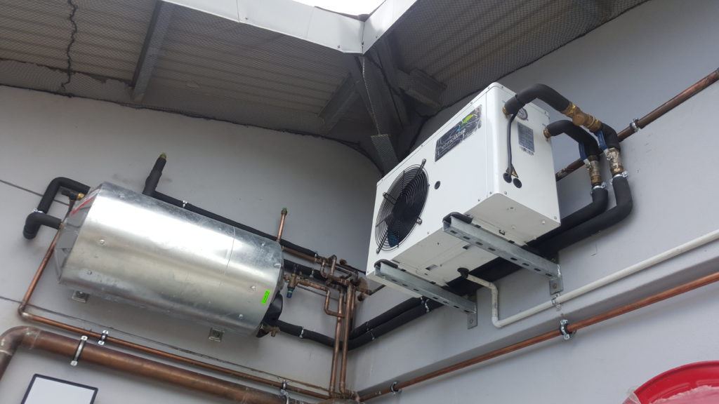 A hot water heat pump and a stainless steel geyser mounted on a wall, joined by insulated and copper pipework